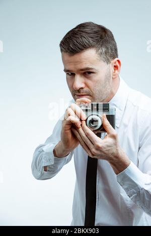 Handsome man in white shirt with black tie, taking a picture with vintage photo camera. Close-up front portrait against bright clean background Stock Photo