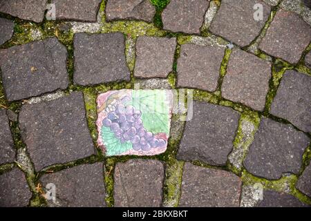 Close-up of a porphyry cubes street pavement in the historic centre of Bardolino with a hand painted decoration representing a bunch of grapes, Italy Stock Photo