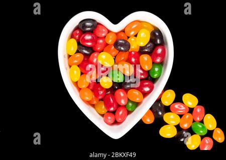 Assorted colorful jelly beans, sweet candy background with a heart-shaped bowl isolated on black. Kids' junk food. Stock Photo