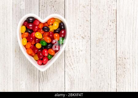 Assorted colorful black, red, green, yellow, and orange jelly beans, sweet candy background with a heart-shaped bowl. Kids' junk food. Stock Photo