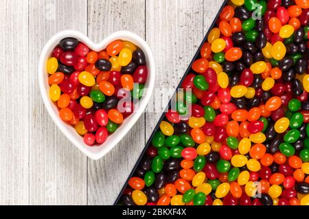 Assorted colorful black, red, green, yellow, and orange jelly beans, sweet candy background with a heart-shaped bowl. Kids' junk food. Stock Photo