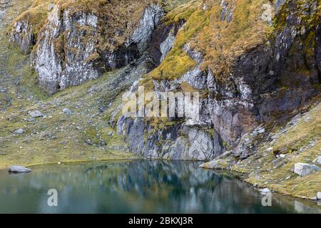 colorful rocky shore mirror reflection in calm Balea mountain lake Stock Photo
