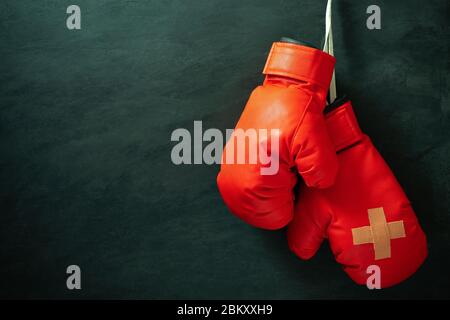 Red boxing gloves hung on black cement wall in darkness with lighting. Adhesive plaster across each other on boxing gloves. Idea of hurt or combat los Stock Photo