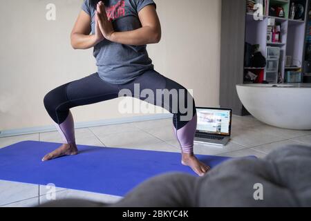 A woman undertaking an online physical fitness exercise lesson within an apartment during a lockdown period of the COVID-19 Pandemic 2020. Stock Photo