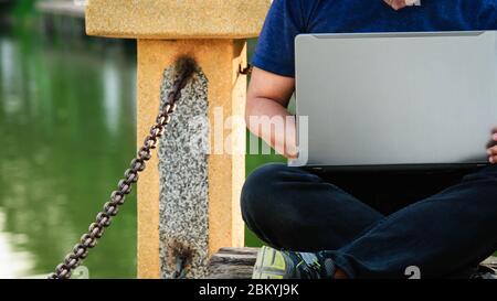 A man were blue shirt who working remotely by using laptop computer in the park. Stock Photo