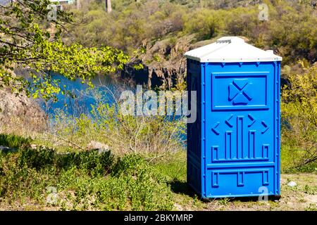 Blue Cabine Of Chemical Toilet In a Mountain Park on a river background at sunny Summer Day. Stock Photo