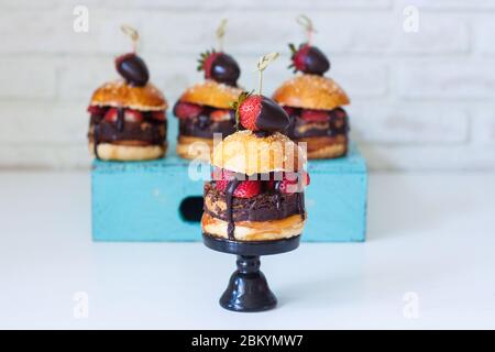 Sweet burger with vanilla bun, brownie layer, strawberries in chocolate and salted caramel. Stock Photo