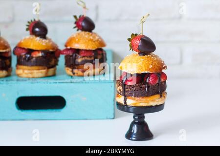 Sweet burger with vanilla bun, brownie layer, strawberries in chocolate and salted caramel. Stock Photo