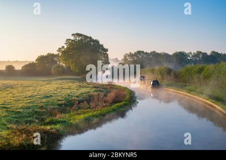 Canal boat in the mist on the oxford canal on a spring morning at sunrise. Near Somerton, Oxfordshire, England