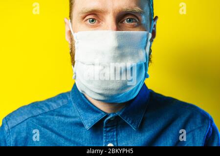 Portrait of a bearded man in a gauze mask on yellow background. Preventive protection of your own health from viral infection. Coronavirus concept. Stock Photo