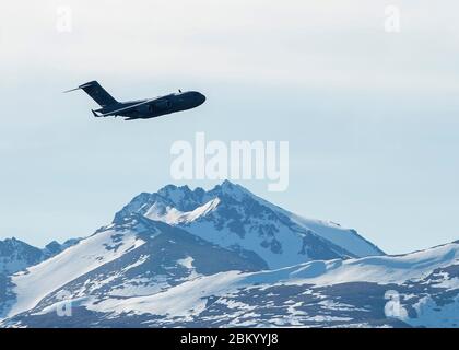 A U.S. Air Force C-17 Globemaster III flies over the flightline at Joint Base Elmendorf-Richardson, Alaska, during a close formation taxi known as an elephant walk, May 5, 2020. This event displayed the ability of the 3rd Wing, 176th Wing and the 477th Fighter Group to maintain constant readiness throughout COVID-19 by Total Force Integration between active-duty, Guard and Reserve units to continue defending the U.S. homeland and ensuring a free and open Indo-Pacific. Stock Photo