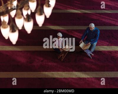 muslim prayer father and son in mosque praying and reading holly book quran together islamic education concept Stock Photo