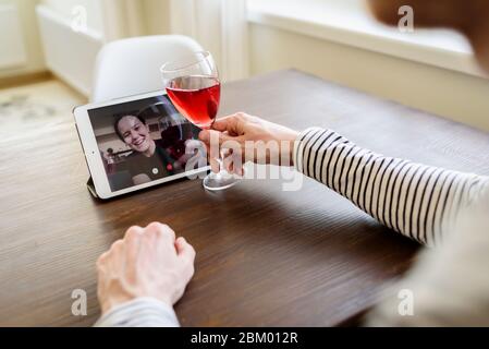 Man drinking red wine online with female friend using tablet pc at home Stock Photo