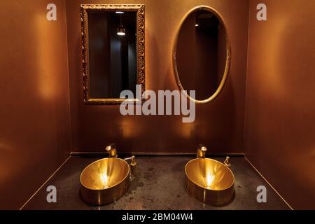 A rectangular and oval mirror  above gold-coloured sinks  in a toilet in a restaurant in Tokyo, Japan. Stock Photo