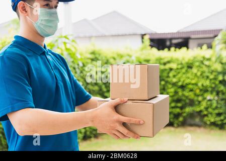 Asian delivery express courier young man use giving boxes to woman customer he wearing protective face mask at front home, under curfew quarantine pan Stock Photo