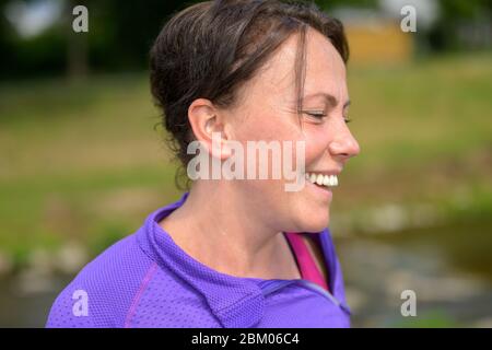 Happy laughing attractive vivacious middle-aged Hispanic woman in a side view portrait outdoors Stock Photo