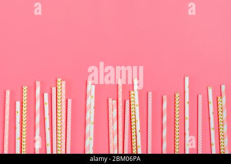 Drinking paper straws for party with golden, white, pink stripes on pink pastel background with copy space. Top view of colorful paper disposable eco Stock Photo