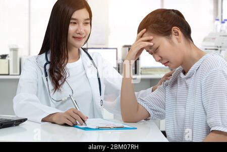 friendly Asian doctor with smiley face, touching stress patient on shoulder for soothe with gently calm in medical consultation room. supporting menta Stock Photo