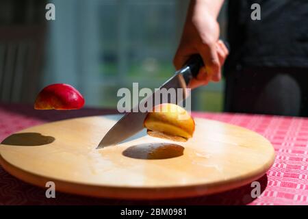 Close up of chef hand chopping apple in half with kitchen knife on the table. Slicing red apple on wooden board Stock Photo