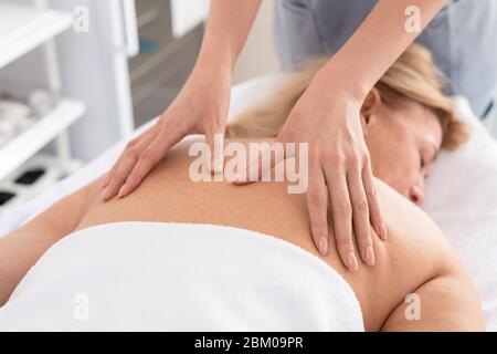 Close-up of unrecognizable therapist giving relaxing back massage to exhausted woman in spa salon Stock Photo