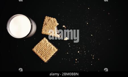 Flat lay of glass of milk with sandwich chocolate biscuits cookies and crumbs on black background copy space Stock Photo
