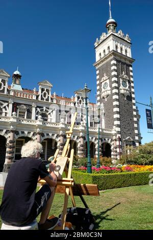 Man doing a pyrography using a magnifying glass in the gardens of Dunedin train station. Stock Photo