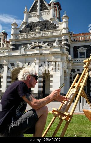 Man doing a pyrography using a magnifying glass in the gardens of Dunedin train station. Stock Photo