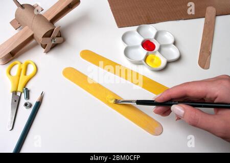 How to make airplane. Hand made toy,zero waste from toilet paper roll and popsicle sticks. For kids and parents. Step 10,paint both wings. Stock Photo