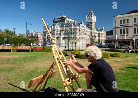 Man doing a pyrography using a magnifying glass in the gardens of Dunedin train station. Stock Photo