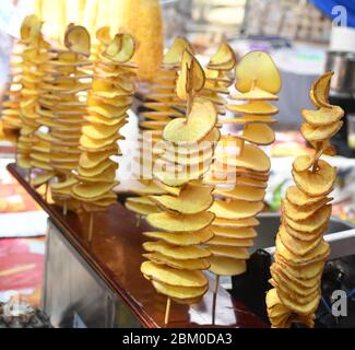 Fried swirl potato spiral on a stick during street food festival. Fast food. Tornado potatoes on a bamboo stick Stock Photo