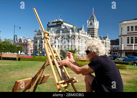 Man doing a pyrography using a magnifying glass in the gardens of Dunedin train station. Stock Photo