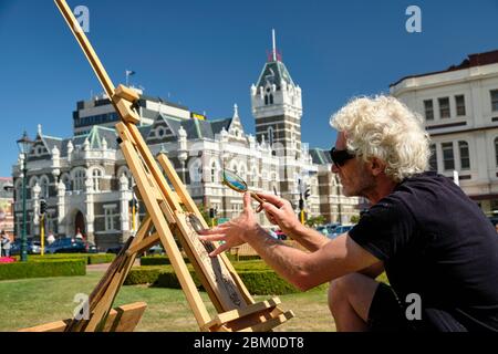 Man doing a pyrography using a magnifying glass in the gardens of Dunedin train station. Stock Photo