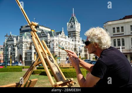 Man doing a pyrography using a magnifying glass in the gardens of Dunedin train station. Stock Photo
