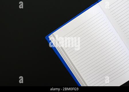 Blue notebook with text lines on white paper, on a not totally black metallic surface. A lot of copy space. (Suggestion: do a horizontal mirror flip t Stock Photo