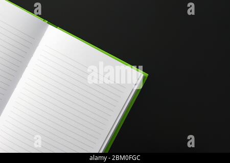 Green notebook with text lines on white paper, on a not totally black metallic surface. A lot of copy space. (Suggestion: do a horizontal mirror flip Stock Photo