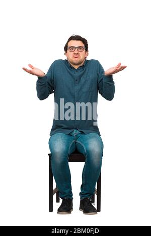 Full length of doubtful businessman, keeps hands outstretched, shrugging shoulders gesture, sitting on a chair isolated on white background. Don't kno Stock Photo