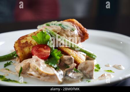Close up of potato hash brown served with chicken, mushrooms, cherry tomato and green needle beans in creamy sauce and pesto. Tasty fresh dish on whit Stock Photo