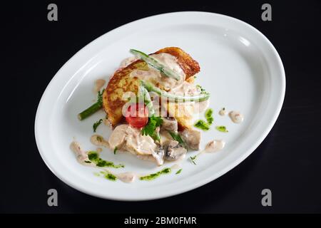 From above view of potato hash brown served with chicken, mushrooms, cherry tomato and green needle beans in creamy sauce and pesto. Tasty fresh dish Stock Photo