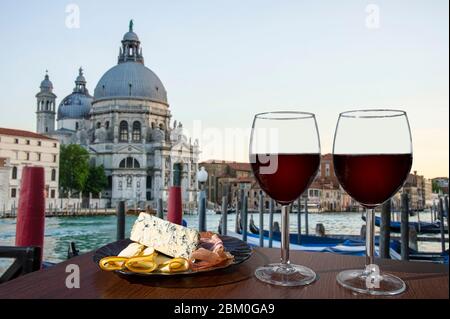Two glasses of red wine with charcuterie assortment on gondolas and Santa Maria della Salute. Glass of red wine with different snacks Stock Photo