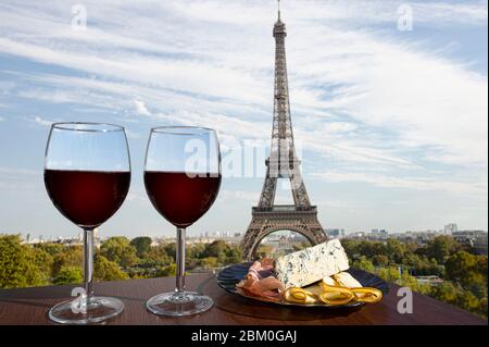 Two glasses of red wine with charcuterie assortment on view of Paris and Eiffel tower background. Glass of red wine with different snacks - plate. Stock Photo