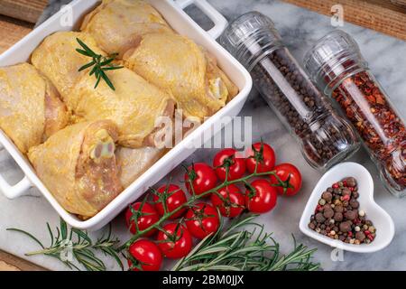 Raw Chicken thigh before cooking.Chicken legs in a yellow marinade in a white baking plate with a branch of razmarin, spices, hot pepper and a branch Stock Photo