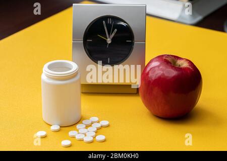 A colorful set of grey alarm clock, red Apple and pill bottles on a bright light yellow background. Medicine of creative concepts. Minimal style with Stock Photo