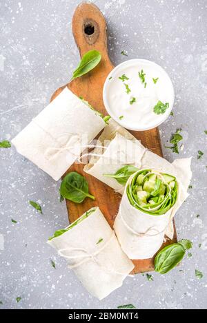 Vegan fresh tortilla wraps with vegetable. Spring fresh pita rolls with tofu, cucumber, baby spinach and avocado. Grey concrete background copy space Stock Photo