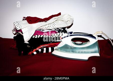 Stack of colorful cotton clothes and iron. Household laundry ironing isolated. Stock Photo