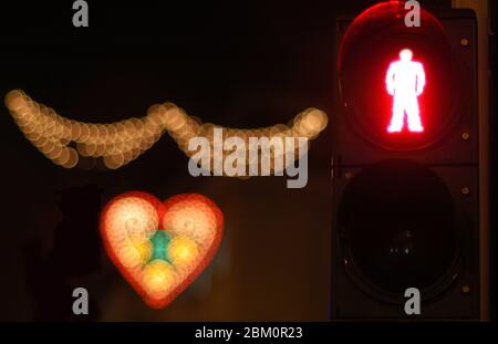 Nighttime photo of a red traffic light for pedestrians next to decorative heart shaped lamps Stock Photo
