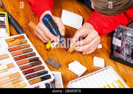 master closes a scratch on the laminate, restoration parquet with wax close-up. repairs. Stock Photo