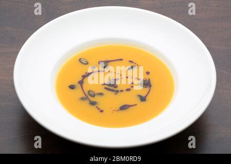 Yellow pumpkin soup in a white ceramic plate on a wooden table Stock Photo