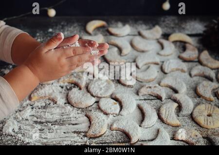 A child sprinkles powdered sugar cookies. Children's hands and flour. Baby is preparing Christmas cookies. Cute baby hands. Baby and cookies. Stock Photo