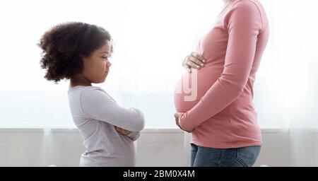 Little Black Girl Looking At Her Pregnant Mom's Belly With Jealousy Stock Photo