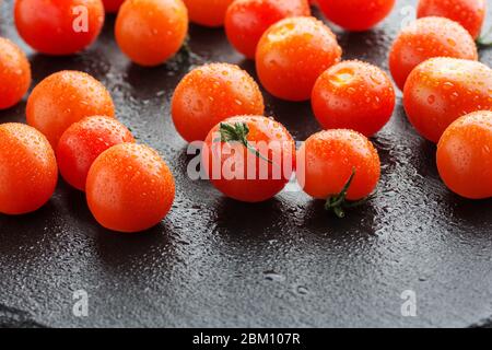Fresh cherry tomatoes on a black slate background with water drops. Minimal black Stock Photo